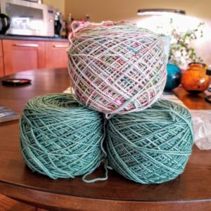 three stacked yarn cakes, two pale green, one multi-speckled white