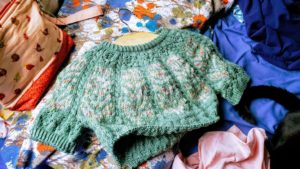 a pastel green colorwork sweater laid flat on a patterned pillowcase