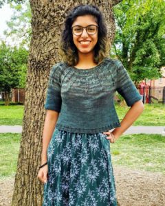 shelly wears a cropped green sweater with textured yoke over a patterned dress